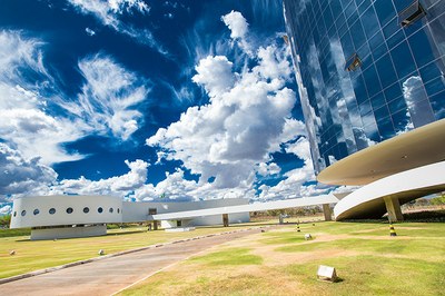 Foto de parte do prédio da PGR, tendo o céu bem azul e reflexo das nuvens nos vidros da edificação