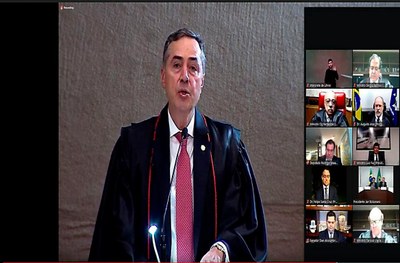 Foto mostra momento da posse do ministro Roberto barroso como presidente do TSE. O ministro está à esquerda, falando ao microfone e os convidados aparecem à direita, em telas quadradas.