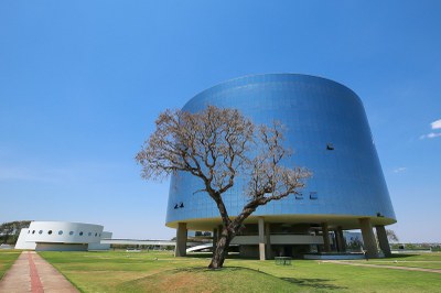 Foto de um dos prédios que abrigam a procuradoria-geral da república, em brasília. o prédio é redondo e revestido de vidro. Há uma árvore à frente.