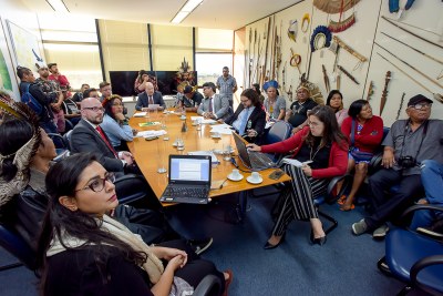 Foto mostra os participantes da reunião, sentados em volta de uma mesa retangular