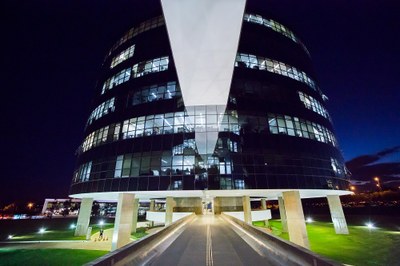 foto noturna de um dos prédios que abrigam a procuradoria-geral da república, em Brasília. O prédio é redondo e revestido de vidro.