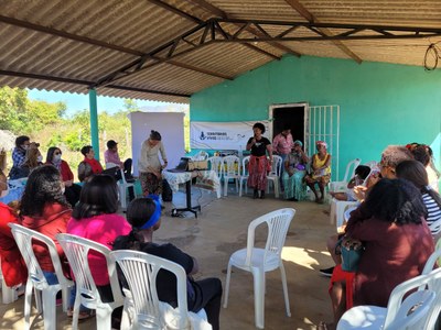 Foto dos participantes da reunião em círculo ouvindo uma mulher que está ao microfone 