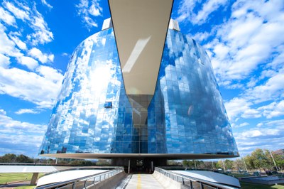 Foto de um dos prédios que abrigam a procuradoria-geral da república, em brasília. O prédio é redondo e revestido de vidro, que reflete as brancas nuvens.