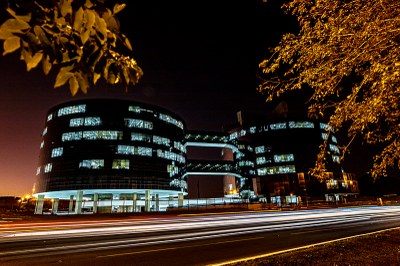Foto noturna dos prédios que abrigam a procuradoria-geral da república, em brasília. os prédios são redondos, interligados e recebem iluminação. à frente dos prédios há galhos de árvores.