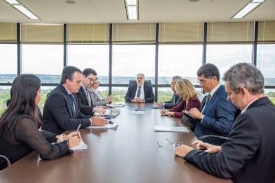 Foto mostra os participantes da reunião, sentados em uma mesa retangular