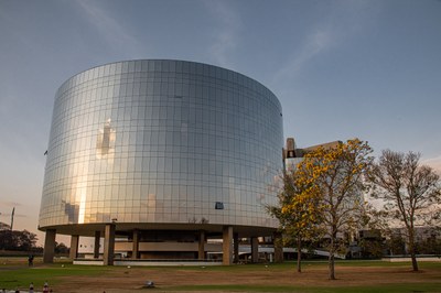 Foto de fim de tarde de um dos prédios que abrigam a procuradoria-geral da república, em brasília. O prédio é redondo e revestido de vidro. Há árvores ao lado da edificação.