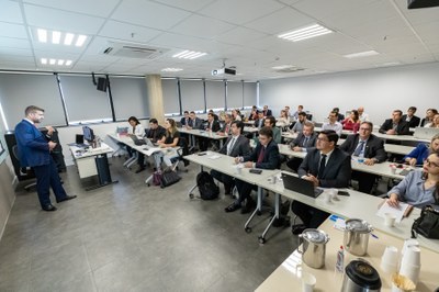 Foto mostra o instrutor à frente, e os participantes do curso sentados em carteiras como uma sala de aula convencional.