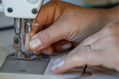 foto de uma máquina de costura e a mão de uma mulher em close costurando