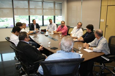 Foto mostra uma reunião com onze homens sentados ao redor de uma mesa. Um deles escreve em um computador.