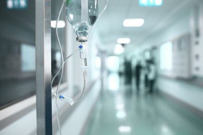Imagem desfocada do corredor de hospital, com destaque para um tubo de soro pendurado em um suporte