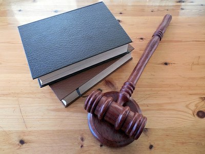 Imagem do martelo da Justiça ao lado de dois livros, empilhados, sobre uma mesa de madeira. 