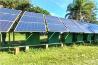 Fotografia da visita à comunidade indígena Guarauaçu Sambaqui em Pontal do Paraná, com painéis de placas solares montados em um campo com vegetação ao fundo