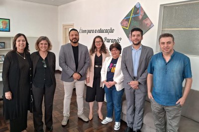 Foto de sete pessoas posando, de pé, com parede ao fundo com a inscrição "é bom para a educação do Paraná?"