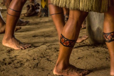 Foto em plano fechado mostra pernas de indígenas ostentando pintura decorativa tradicional.