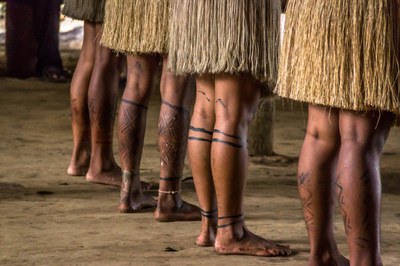 Foto mostra pernas de indígenas pintadas, vestidas com saias de palha 