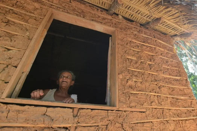 Foto de uma mulher quilombola na janela de uma casa com parede de barro e telhado de palha



