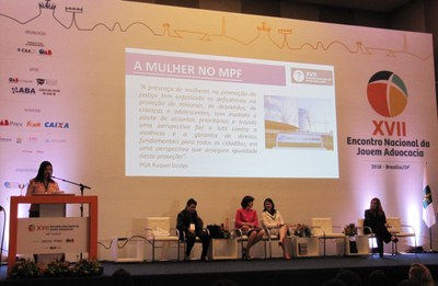 Foto mostra a procuradora-chefe da PRR1 Valquíria Quixadá discursando, com projeção ao fundo onde se lê o tema da palestra: A mulher no MPF. 