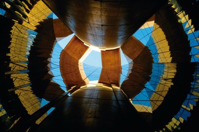 Imagem de um ângulo pouco usual do prédio da PGR, em Brasília. Foto mostra parte de uma das colunas da estrutura sendo refletia pela pele de vidro da edificação, formando uma espécie de espiral com a mistura das luzes azuis, amarelas e reflexos pretos.