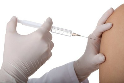 A foto focou em duas mãos com luvas brancas aplicando vacina no braço de uma pessoa. 