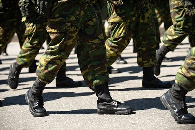 Imagem mostra pessoas da cintura para baixo, com uniforme militar e marchando.