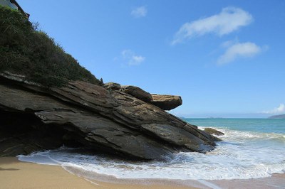 Imagem da Praia das Caravelas com seus costões rochosos ao lado esquerdo e o mar, do lado direito.
