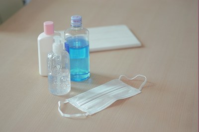 Foto de um kit contendo álcool em gel, máscara, sabão, em cima de uma mesa de madeira 