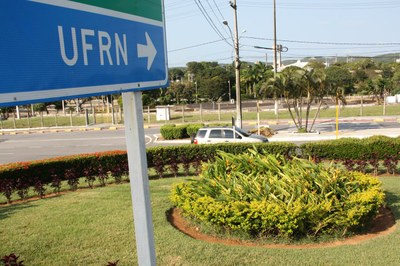 Placa de trânsito apontando para a UFRN, aparecendo jardim da universidade
