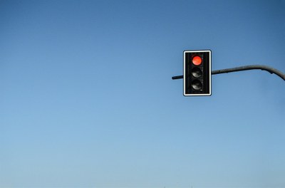 Foto de semáforo com a luz vermelha acesa, tendo ao fundo céu azul