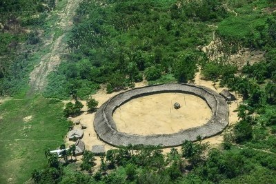Foto aérea mostra oca indígena, construção com telhado de palha em formato circular, em meio a floresta. 