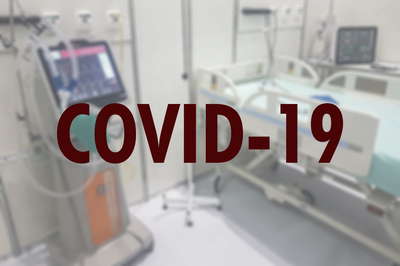 #Pracegover Foto de cama de hospital desfocada, com a palavra COVID-19 em vermelho escuro