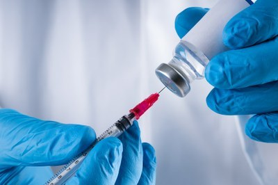 Imagem de mão com luva manipulando uma vacina