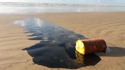 grande mancha de óleo e barril de metal na beira da praia