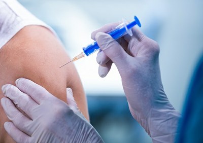 fotografia das mãos de um profissional de saúde aplicando vacina no braço de um homem branco