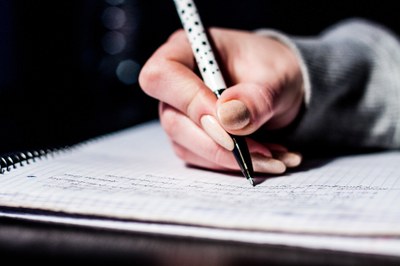 #Paratodosverem: imagem mostra mão direita feminina escrevendo com caneta sobre uma folha de caderno