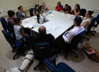 Imagem da reunião realizada na sede do MPF em São Paulo. Participantes estão sentados à mesa, com a presença de dois cães-guia ao lado.