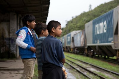 Foto mostra pequenos indígenas observando um trem passando em frente à estação